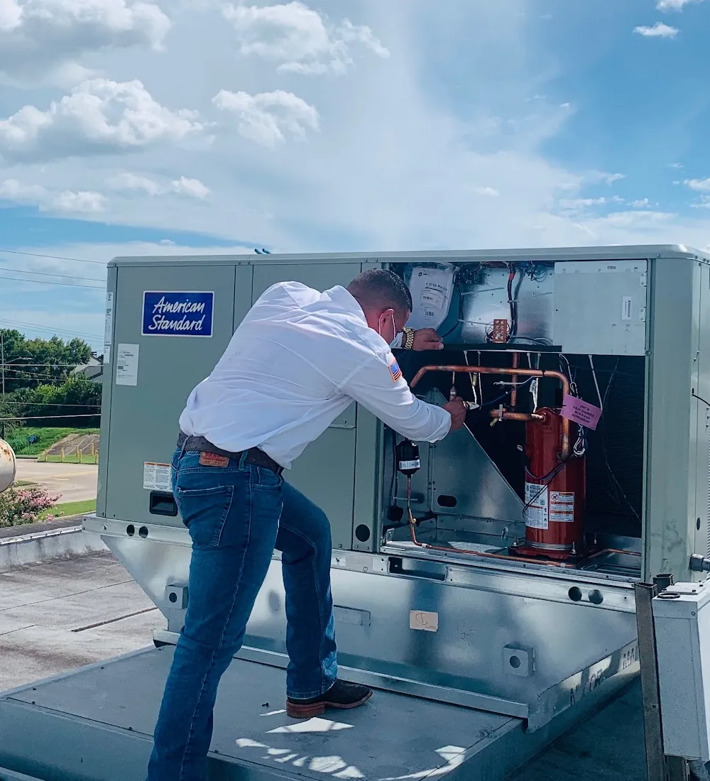 A technician working an opened rooftop package unit under open sky